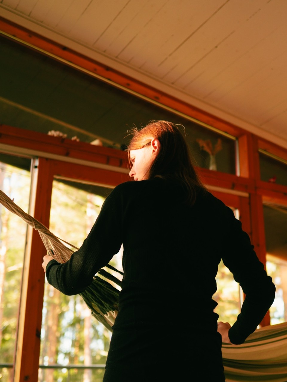 Woman in black setting up a hammock in a sunlit cabin