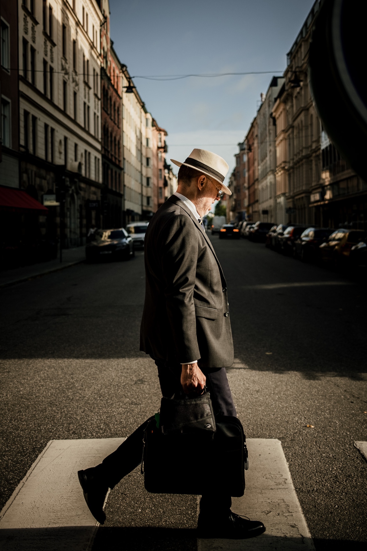 Man in a grey suit and hat crossing a sunlit street