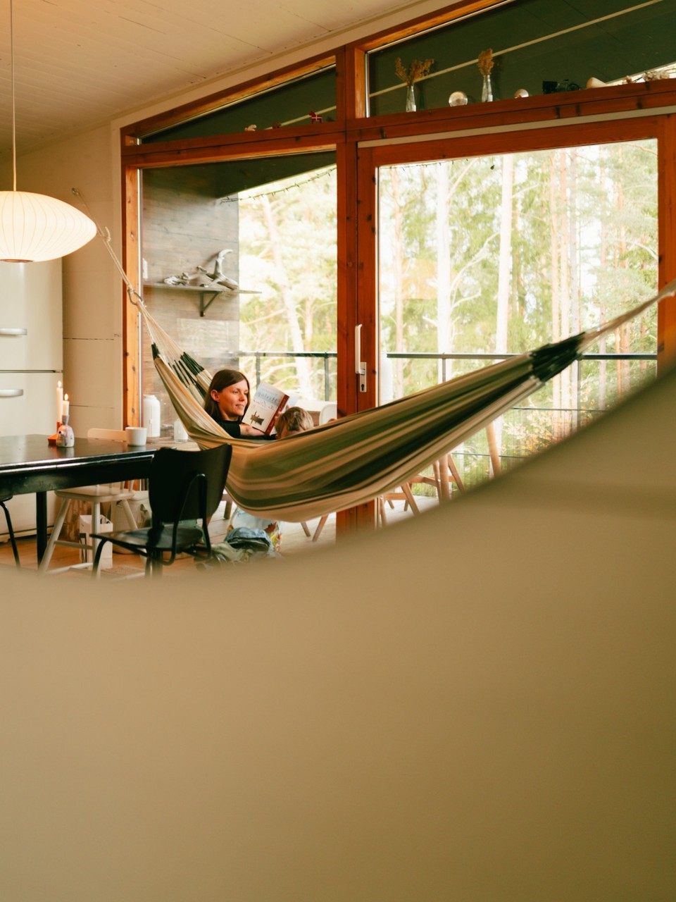 Woman reading to a child in a hammock by wide windows
