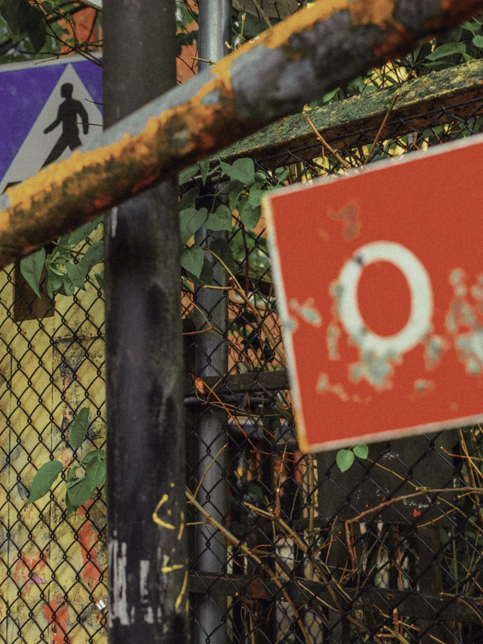 Rusted railing and faded signs on an overgrown chain-link fence