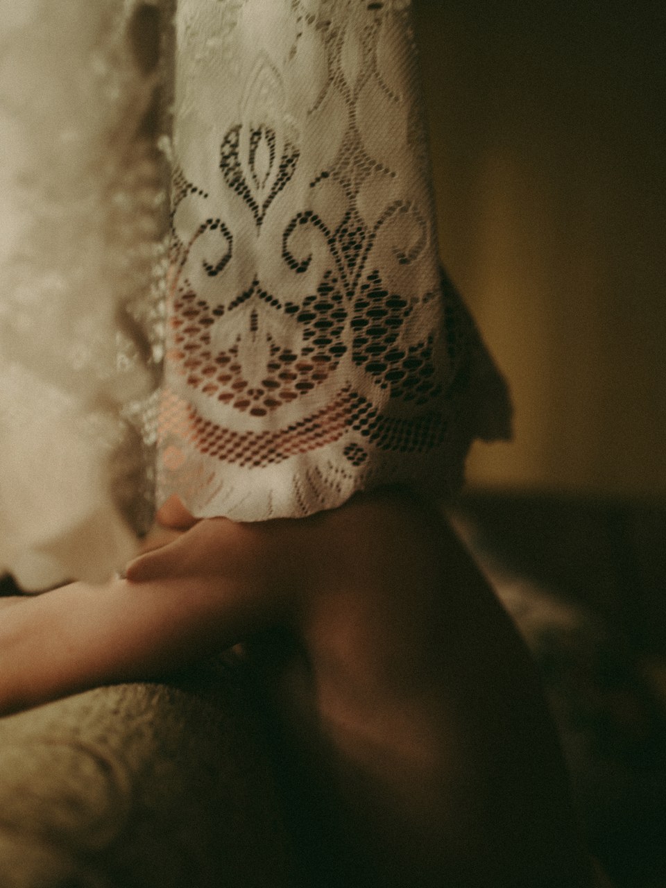 Hand resting beneath the edge of a white lace curtain