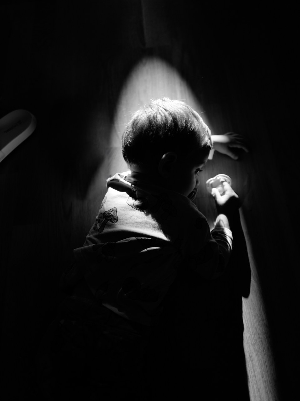 Baby crawling through a beam of light on a dark floor, black and white